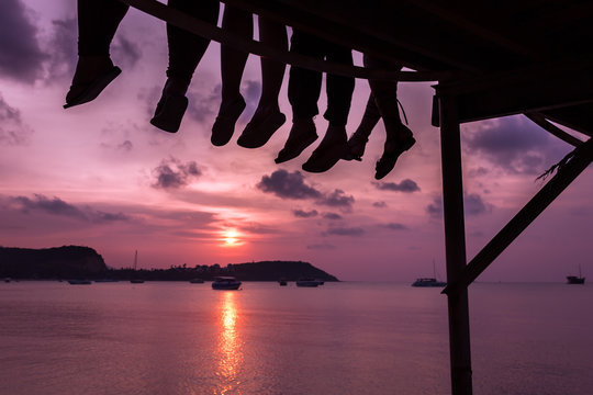 Group of friends sitting on the dock of the bay enjoying lovely sunset in the island of Koh Samui, Thailand