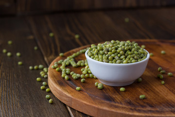 Organic mung beans on white ceramic bowl over wooden background.
