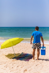 Fototapeta na wymiar Young man with ice bar cooler under solar umbrella on a beach near ocean