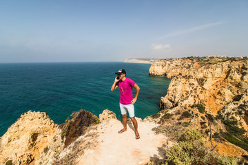 Fototapeta premium Man in end of the rock near atlantic ocean speak on phone on summer sunny days