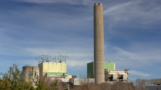 Cape cod canal power plant against blue sky and wispy clouds with trees in foreground.