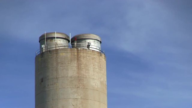 Zoomed shot of power plant smoke stack with no belching smoke against blue sky and wispy clouds.