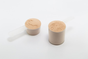 heap of isolate and chocolate protein powder with plastic spoon on white background