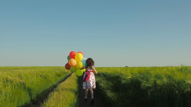 Child with balloons in the field. A little girl on a country road with inflatable balls.