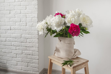 Still life with a bouquet of peonies in a vase on a wooden stool.