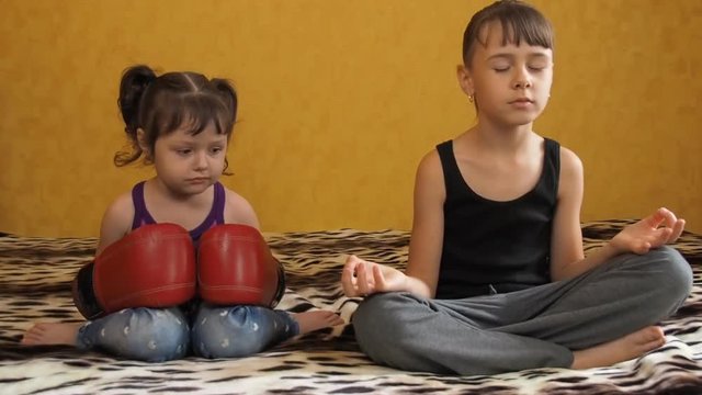 Two sisters go in for sports. A little girl in boxing gloves. The girl is engaged in yoga.