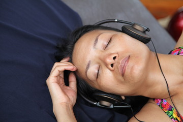 relaxed asian woman enjoying listening the music with headphones close eyes sleeping on summer