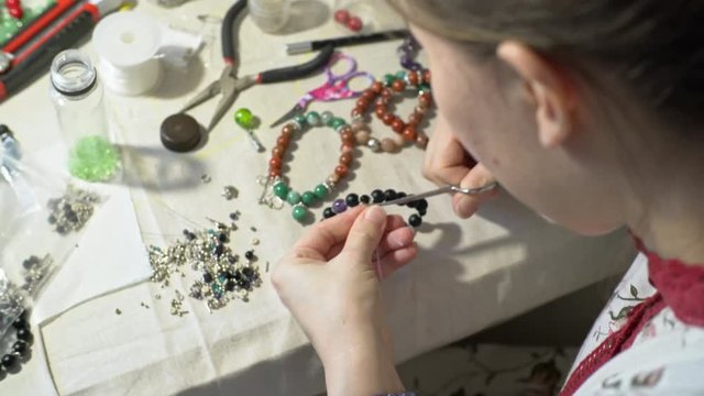 Top view of young woman tying handmade beads bracelet and cutting excess string