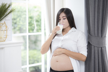 Young asian pregnant woman drinking milk and  showing her belly and carefully holding.