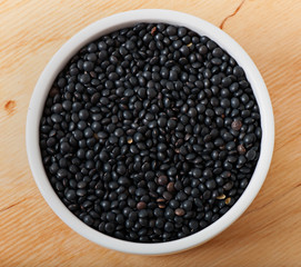 Lentil seeds on a white plate, on an old wooden background.