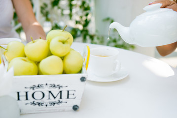 Tea drinking. White kettle on the table. Green tea and green apples in the basket. No trendmark.  Drink tea in a summer cafe. Selective focus
