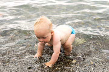 First steps in the sea. Funny kid boy trying to walk in the water