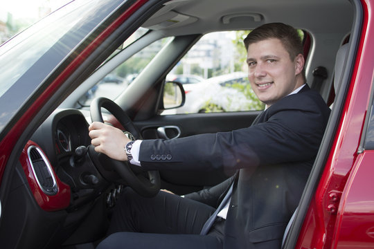 Businessman sitting in his car in a parking lot. Looking at the camera with open car doors. Suit and tie businessman sitting in his automobile.