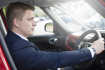 Businessman sitting in his car in a parking lot. Looking at the distance with open car doors. Suit and tie businessman sitting in his automobile.