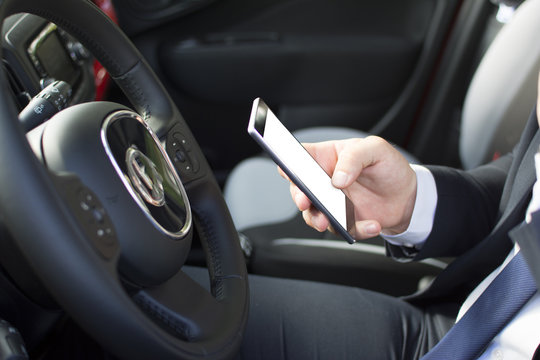 Close-up of a man's hand holding a smartphone. Businessman texting while sitting in a parking lot. Suit and tie man using a mobile phone.