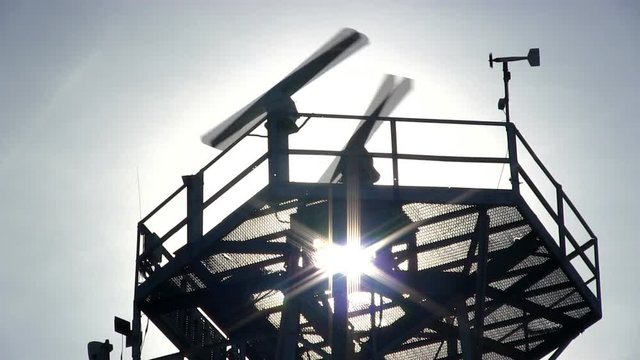 Marine traffic control radar tower silhouette close-up with spinning antenna and wind sensor