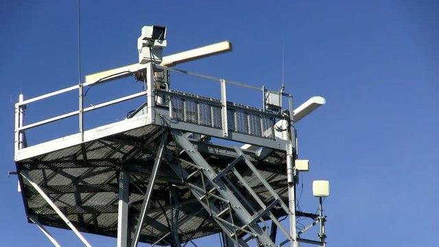 Spinning radar antenna on marine traffic control tower with surveillance camera against blue sky