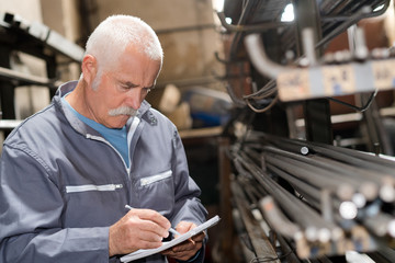 Senior man noting stock of metal rods