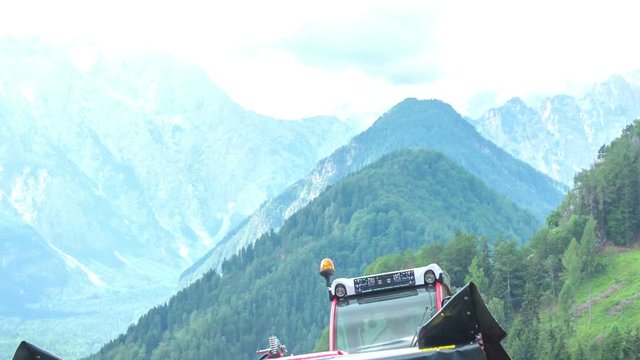 A tractor stops driving on the top of the hill. There are beautiful high mountains in the background.