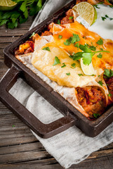 Mexican food. Cuisine of South America. Traditional dish of spicy beef enchiladas with corn, beans, tomato. On a baking tray, on old rustic wooden background. Copy space