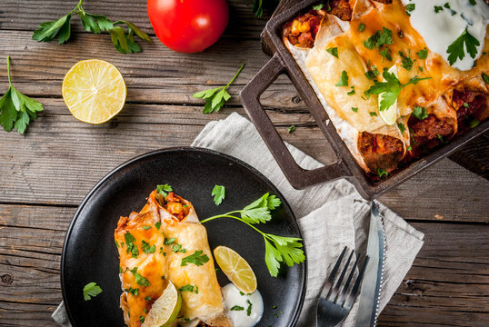 Mexican food. Cuisine of South America. Traditional dish of spicy beef enchiladas with corn, beans, tomato. On a baking tray, on old rustic wooden background. Copy space top view