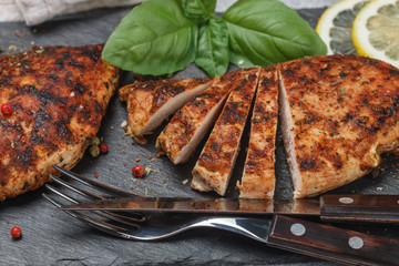 Delicious grilled chicken fillet with herbs and spices on black slate plate close up