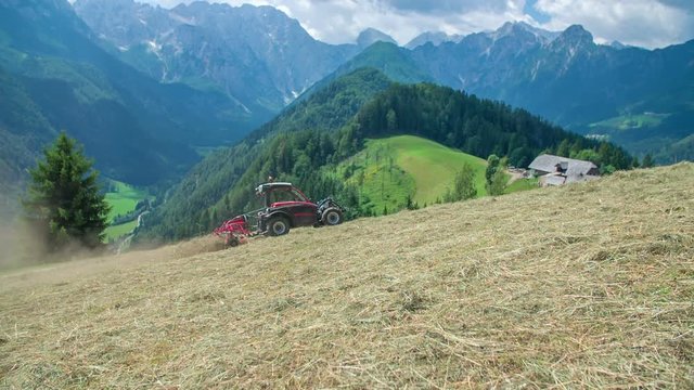 A farmer is working on the field on a hot summer day and is preparing hay. The scenery behind it is gorgeous.