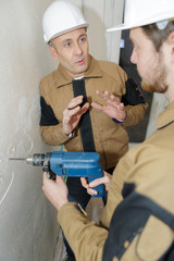 builder and apprentice using power tool on site