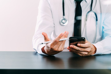 close up of smart medical doctor working with smart phone and stethoscope on dark wooden desk with glass reflected view