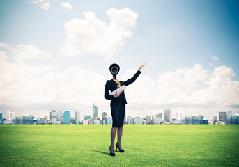 Camera headed woman standing on green grass against modern citys