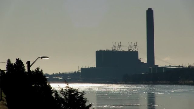 Distant shot of power plant silhouette along quite canal as birds chirp in early spring morning stillness.