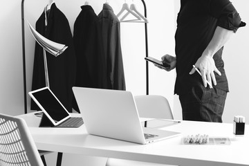 Fashion designer talking mobile phone and using laptop with digital tablet computer in modern studio