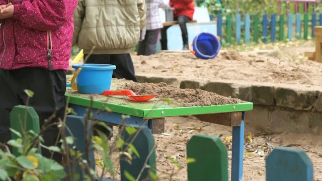 Children playing with sand on green table in kindergarten outdoor