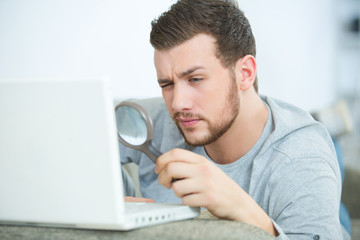 man looking at laptop through magnifying glass