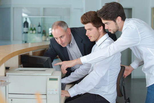 Three men looking at computer screen behind reception desk