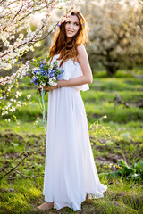 Beautiful girl with long hair in a white dress in a flowery garden with flowers
