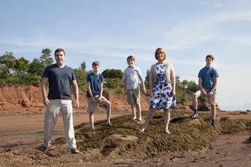  a family in casual summer clothes poses on a rock looking out at the beach