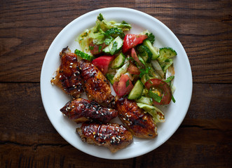 Sweet teriyaki chicken wings with vegetable salad in a plate top view