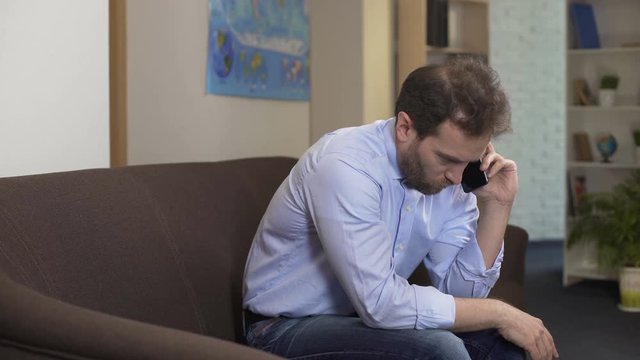 Upset male sitting at home and chatting with ex-wife on smartphone, problems