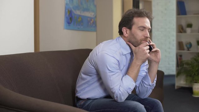 Sad man sitting on sofa and talking with boss on smartphone, problems and crisis