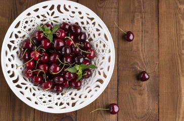 Fototapeta na wymiar Ripe sweet cherry with mint on a laсe bowl. Wooden Background. Flat lay. Top view