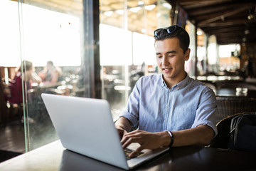Portrait of handsome asian smiling man using laptop in the cafe