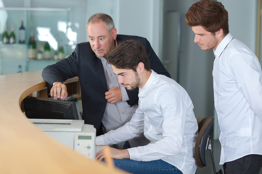 Three men looking at computer behind reception desk