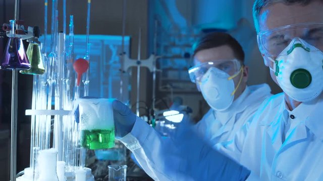 Group of chemists working in a laboratory conducting scientific tests using coolorful chemical solutions in assorted glassware and wearing sterility masks