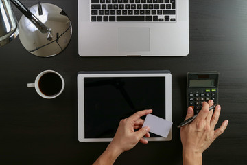 Internet shopping concept.Top view of hands working with calculator and laptop and credit card and tablet computer on dark wooden table background