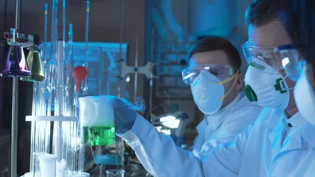 Crop group of chemists working in a laboratory conducting scientific tests using coolorful chemical solutions in assorted glassware and wearing sterility masks