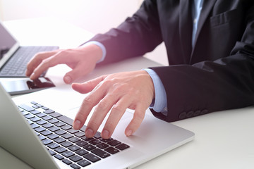 Hands of businessman typing on laptop in modern office with smart phone and digital tablet computer