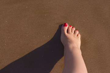 Feet of woman with nails painted red on the sand of the sea