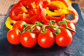Tomatoes on a branch and peper rings on a dark board