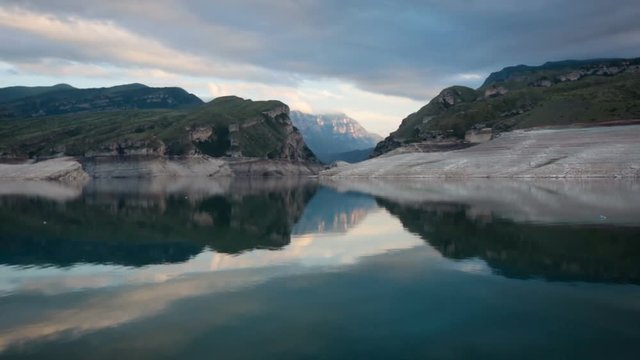 Mountain Lake in Remote Area. Green Rock Hills. Water Streaming Down in Canyon. Mirror Reflection of Cloudy Sky on River Surface. Summer Evening